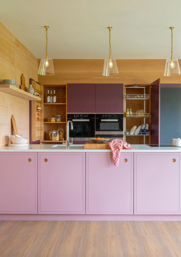 Cette image montre une petite cuisine parallèle design avec un évier 1 bac, un placard à porte plane, des portes de placard violettes, un plan de travail en quartz, un électroménager en acier inoxydable, un sol en bois brun, un sol marron, un plan de travail blanc et une péninsule.