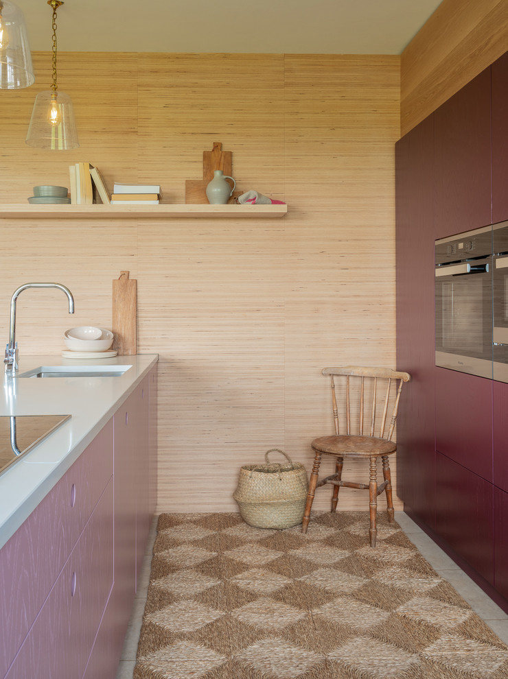 Cette image montre une petite cuisine design avec un évier 1 bac, un placard à porte plane, des portes de placard violettes, un plan de travail en quartz, un électroménager en acier inoxydable, un sol en bois brun, îlot, un sol marron et un plan de travail blanc.