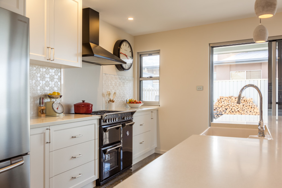 Modern inredning av ett mellanstort kök, med en nedsänkt diskho, luckor med infälld panel, vita skåp, laminatbänkskiva, vitt stänkskydd, stänkskydd i keramik, svarta vitvaror, betonggolv och en köksö