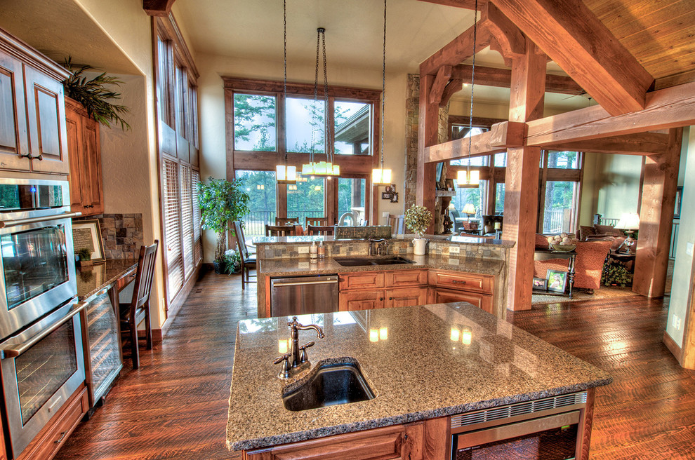 Inspiration for a large craftsman l-shaped medium tone wood floor open concept kitchen remodel in Seattle with an undermount sink, raised-panel cabinets, medium tone wood cabinets, granite countertops, brown backsplash, stone tile backsplash, stainless steel appliances and an island