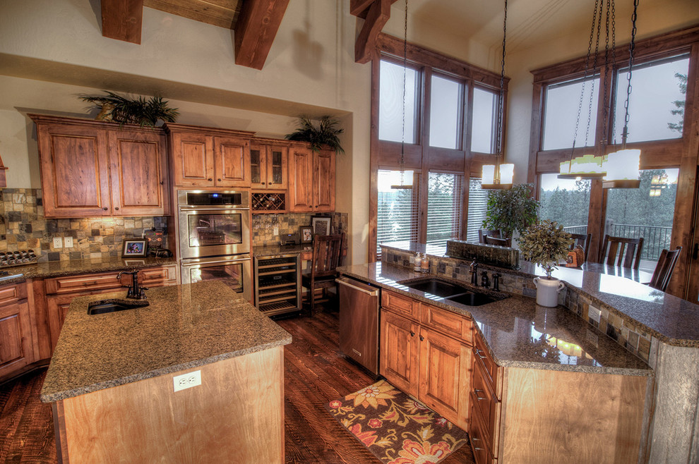 Bild på ett stort amerikanskt kök, med en undermonterad diskho, luckor med upphöjd panel, skåp i mellenmörkt trä, granitbänkskiva, brunt stänkskydd, stänkskydd i stenkakel, rostfria vitvaror, mellanmörkt trägolv och en köksö