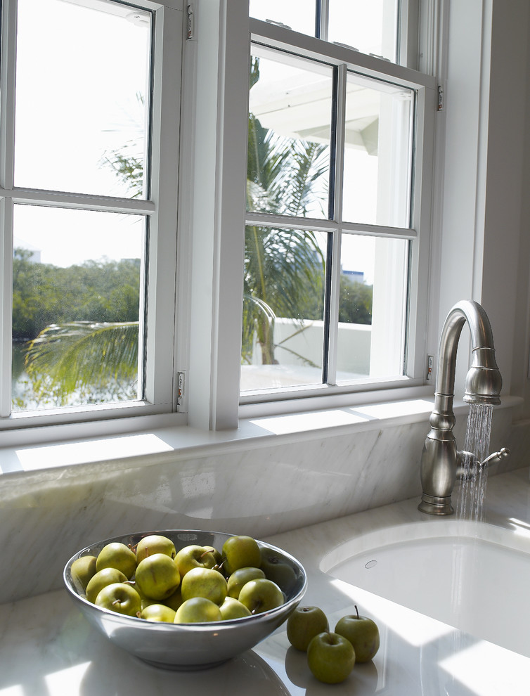 Foto di una grande cucina tropicale con lavello sottopiano, ante con riquadro incassato, ante con finitura invecchiata, top in marmo, paraspruzzi bianco, paraspruzzi in lastra di pietra, elettrodomestici da incasso, parquet scuro e pavimento marrone