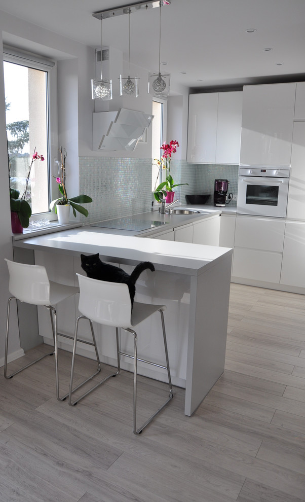 Inspiration for a small contemporary u-shaped enclosed kitchen in Other with a single-bowl sink, flat-panel cabinets, white cabinets, laminate countertops, metallic splashback, mosaic tiled splashback, white appliances, light hardwood flooring and an island.