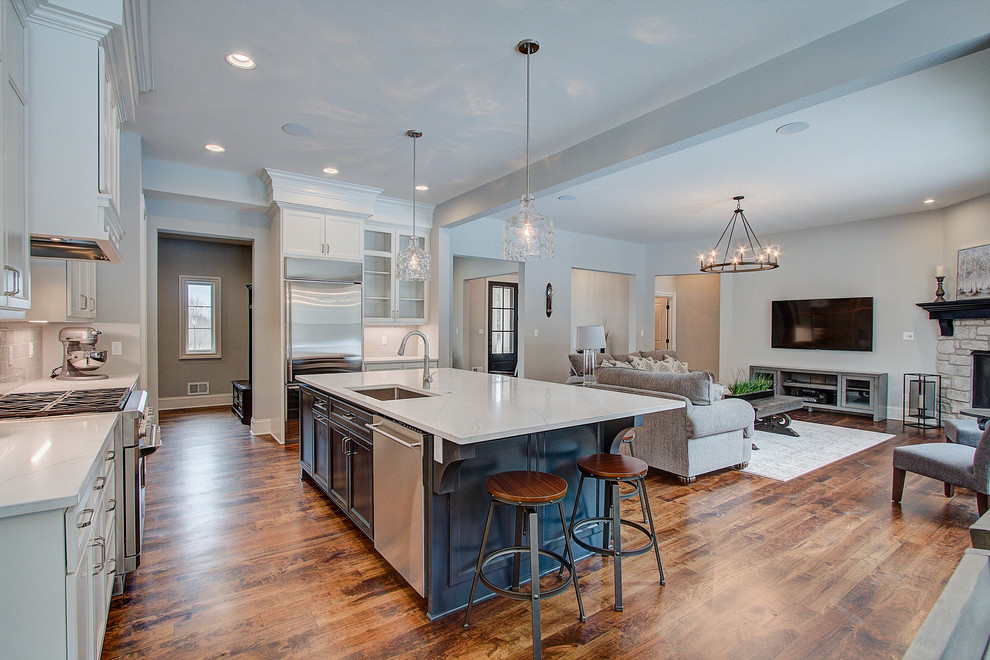 Example of a large classic l-shaped medium tone wood floor and brown floor eat-in kitchen design in Milwaukee with an undermount sink, flat-panel cabinets, white cabinets, quartz countertops, gray backsplash, ceramic backsplash, stainless steel appliances, an island and white countertops