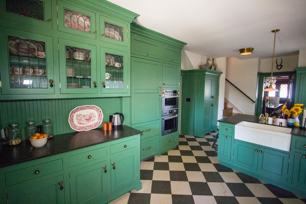 Example of a large arts and crafts l-shaped limestone floor enclosed kitchen design in Los Angeles with a farmhouse sink, shaker cabinets, green cabinets, quartz countertops, green backsplash, white appliances and a peninsula
