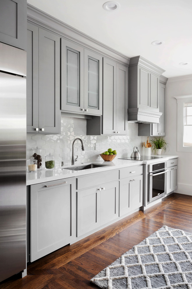 Large transitional single-wall dark wood floor kitchen photo in San Francisco with an undermount sink, shaker cabinets, gray cabinets, solid surface countertops, white backsplash, ceramic backsplash and stainless steel appliances