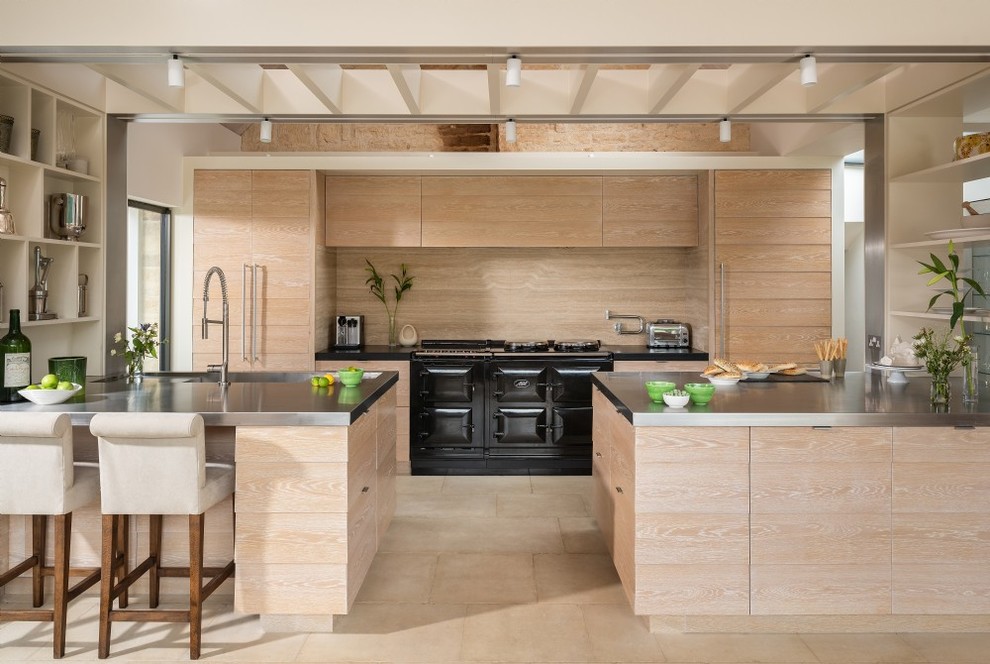 Immagine di una cucina costiera con lavello integrato, ante lisce, ante in legno chiaro, top in acciaio inossidabile, paraspruzzi in legno, elettrodomestici neri, penisola e pavimento beige