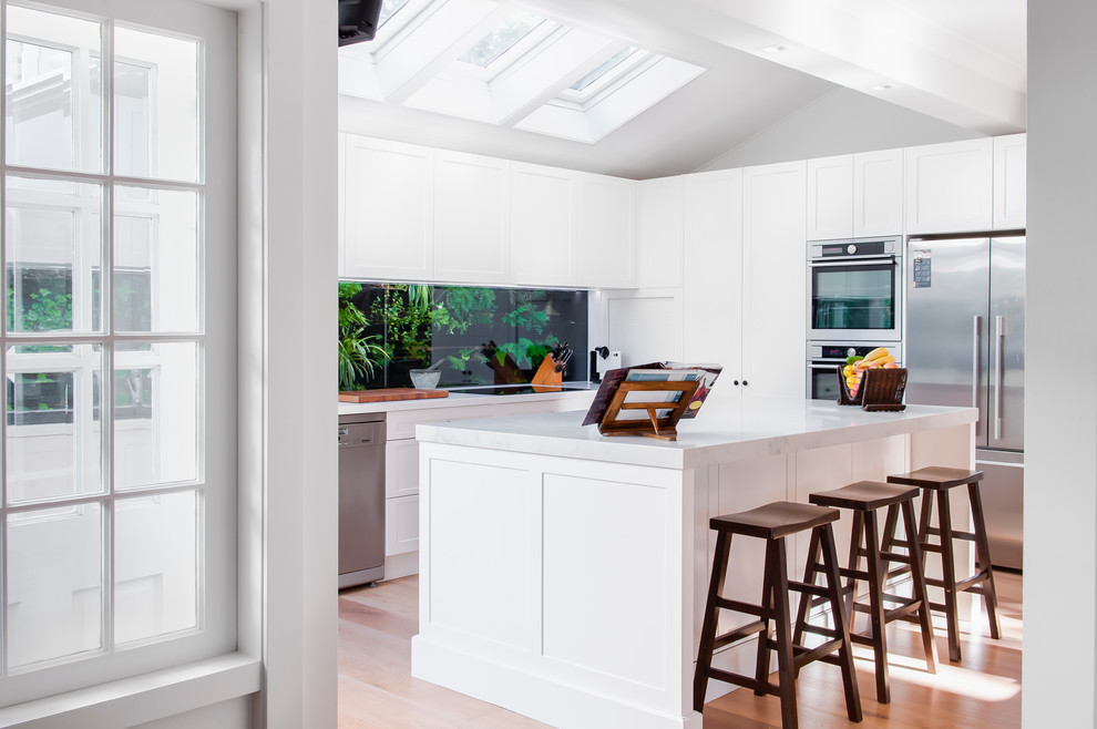 Idée de décoration pour une cuisine américaine minimaliste en L de taille moyenne avec des portes de placard blanches et îlot.