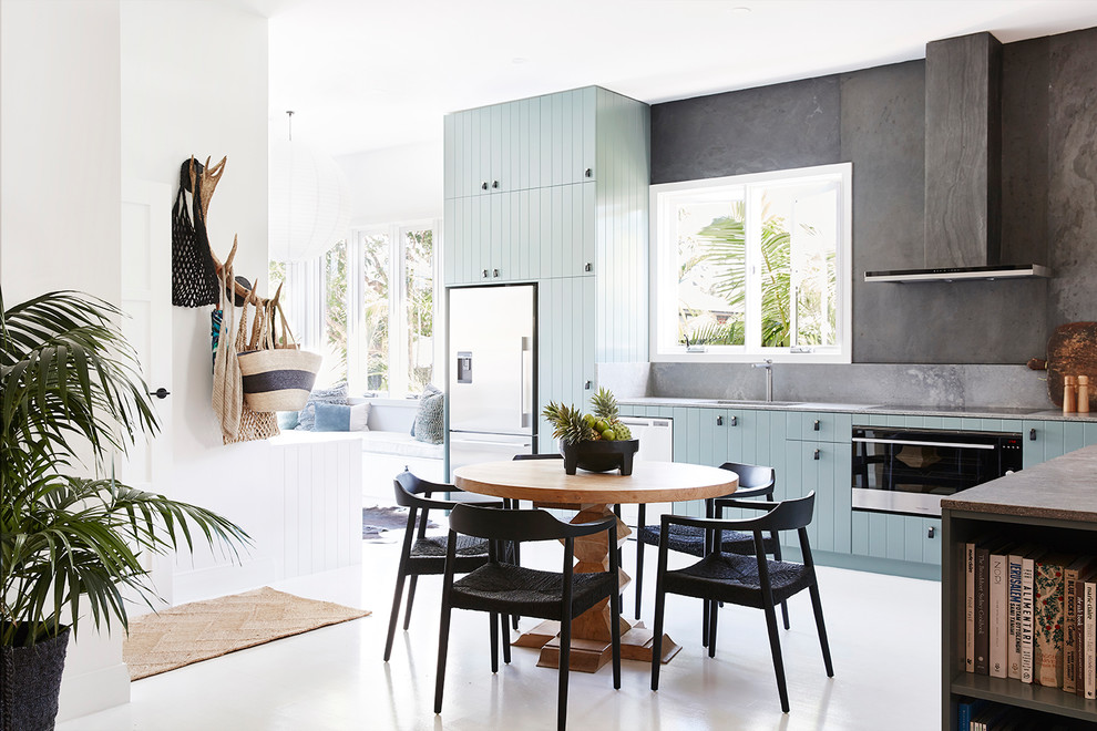 シドニーにある高級な中くらいなトロピカルスタイルのおしゃれなキッチン (アンダーカウンターシンク、フラットパネル扉のキャビネット、クオーツストーンカウンター、グレーのキッチンパネル、スレートのキッチンパネル、シルバーの調理設備、塗装フローリング、白い床、グレーのキッチンカウンター、青いキャビネット) の写真