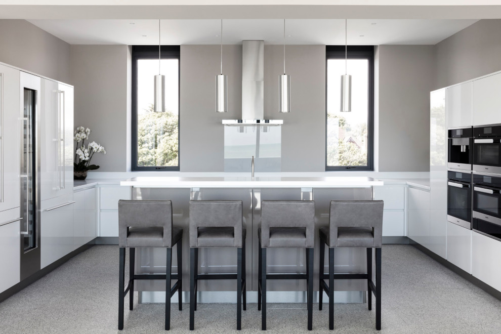 Contemporary u-shaped kitchen in Sussex with flat-panel cabinets, white cabinets, grey splashback, glass sheet splashback, black appliances, an island, grey floors and white worktops.