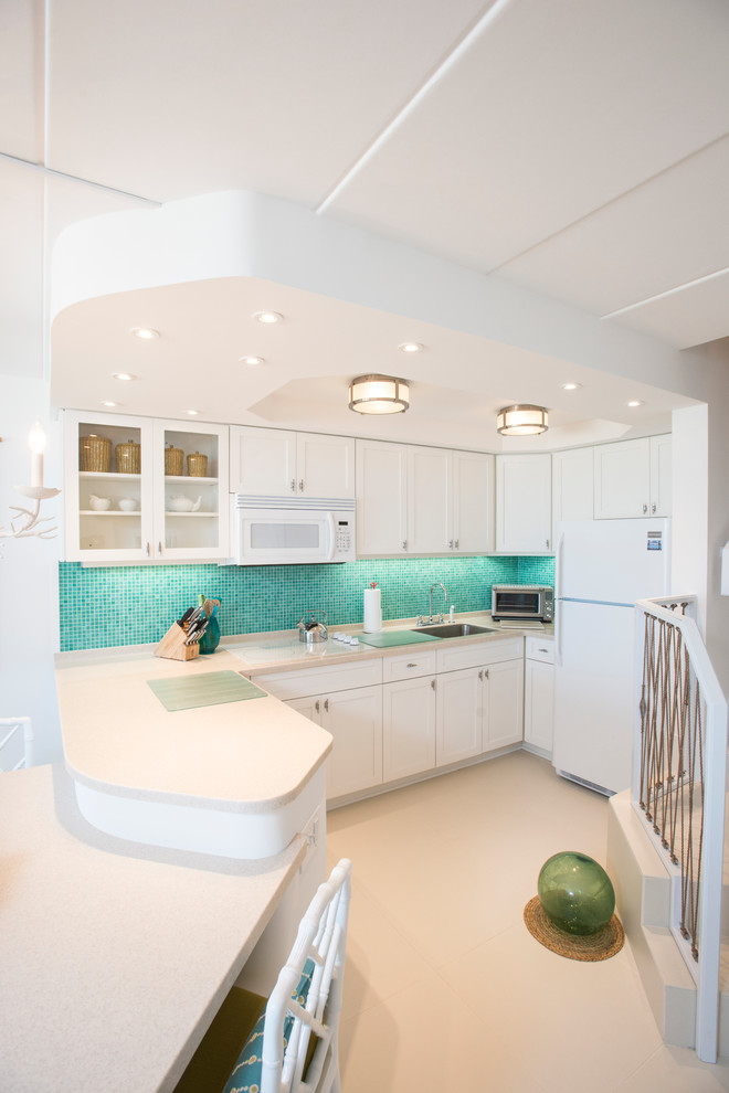 This is an example of a medium sized nautical l-shaped kitchen in Other with a single-bowl sink, recessed-panel cabinets, white cabinets, soapstone worktops, green splashback, glass tiled splashback, white appliances, porcelain flooring, a breakfast bar and beige floors.