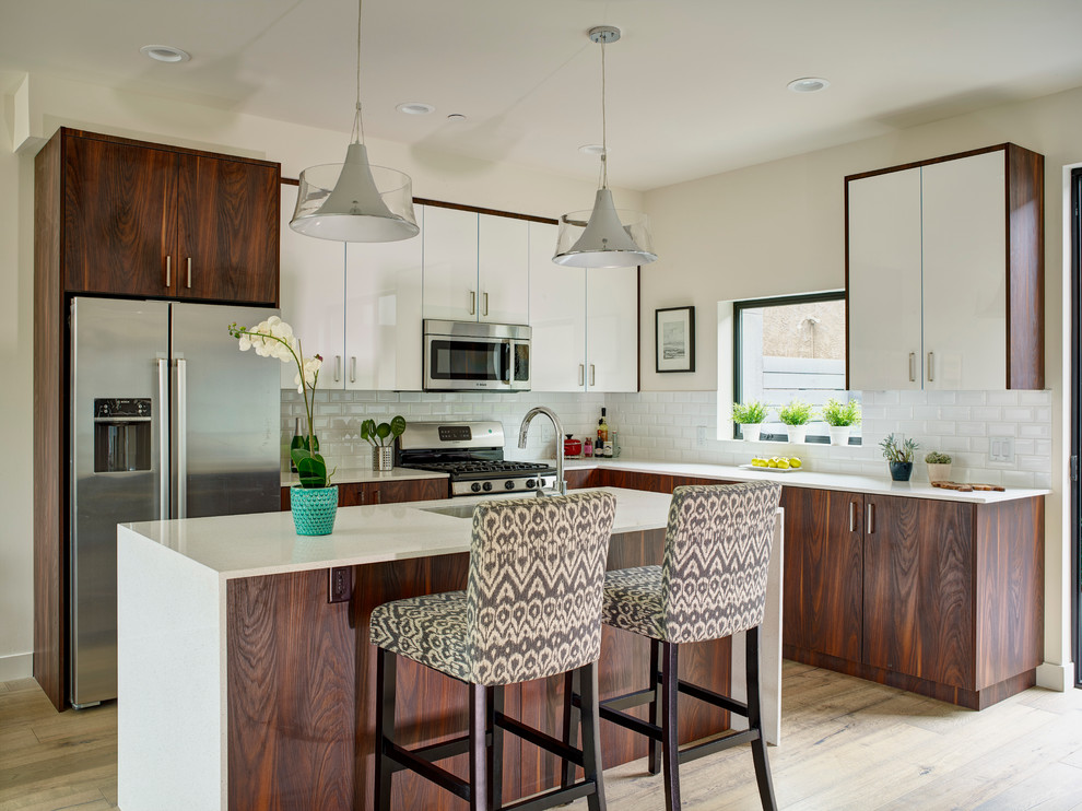 Eat-in kitchen - mid-sized contemporary l-shaped light wood floor eat-in kitchen idea in Los Angeles with flat-panel cabinets, dark wood cabinets, white backsplash, subway tile backsplash, stainless steel appliances, an island, an undermount sink and solid surface countertops