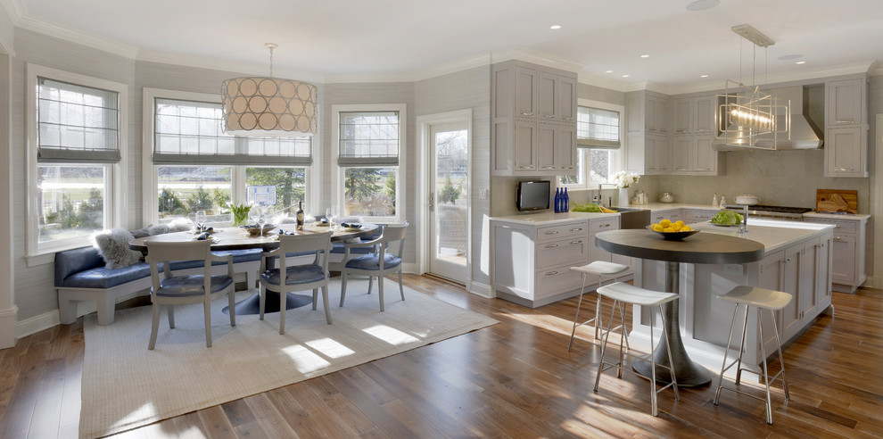 Example of a huge classic u-shaped medium tone wood floor and brown floor eat-in kitchen design in New York with a farmhouse sink, shaker cabinets, gray cabinets, glass countertops, gray backsplash, limestone backsplash, paneled appliances and an island