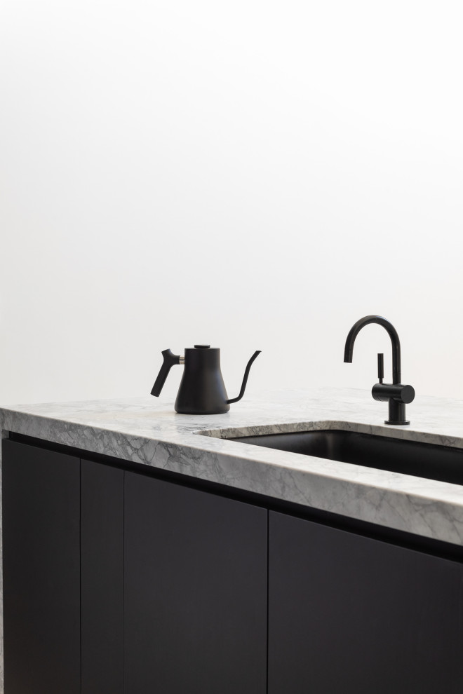 Foto på ett litet funkis grå linjärt kök och matrum, med en enkel diskho, släta luckor, svarta skåp, grått stänkskydd, svarta vitvaror, betonggolv, en köksö och grått golv