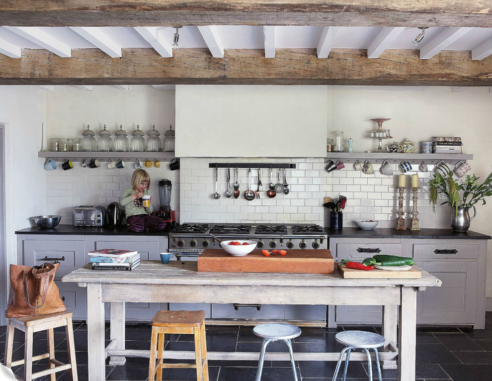 Foto på ett lantligt kök, med öppna hyllor, grå skåp, vitt stänkskydd, stänkskydd i tunnelbanekakel, rostfria vitvaror och en köksö