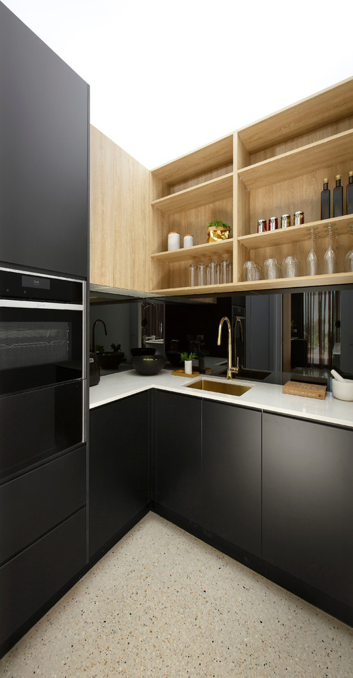 На фото: большая параллельная кухня в стиле модернизм с кладовкой, одинарной мойкой, черными фасадами, столешницей из кварцевого агломерата, фартуком цвета металлик, зеркальным фартуком, черной техникой и островом