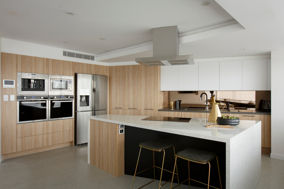 Photo of a large contemporary kitchen in Melbourne with a submerged sink, flat-panel cabinets, metallic splashback, an island, light wood cabinets, mirror splashback and stainless steel appliances.