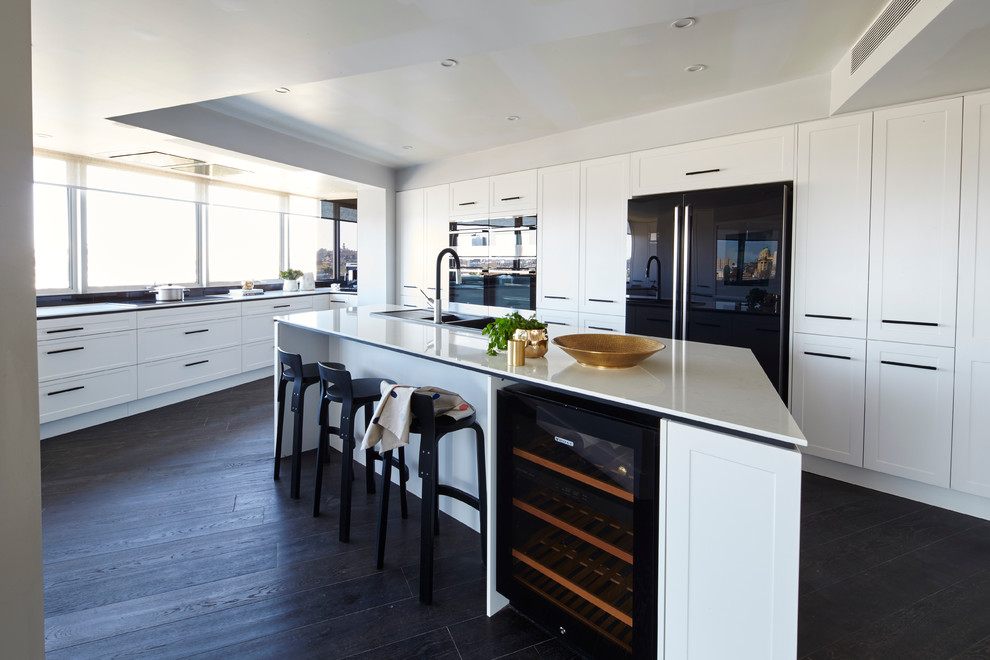 Example of a large trendy dark wood floor and black floor kitchen design in Melbourne with a drop-in sink, recessed-panel cabinets, black appliances and an island