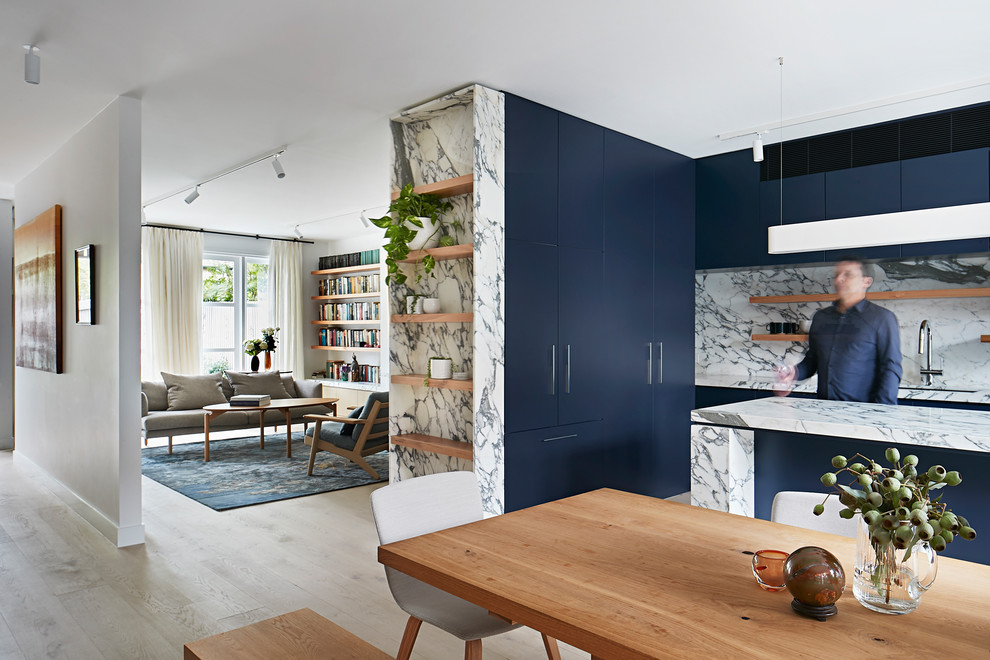 Inspiration for a medium sized modern l-shaped kitchen/diner in Melbourne with a submerged sink, flat-panel cabinets, blue cabinets, marble worktops, white splashback, marble splashback, stainless steel appliances, light hardwood flooring, an island and white worktops.