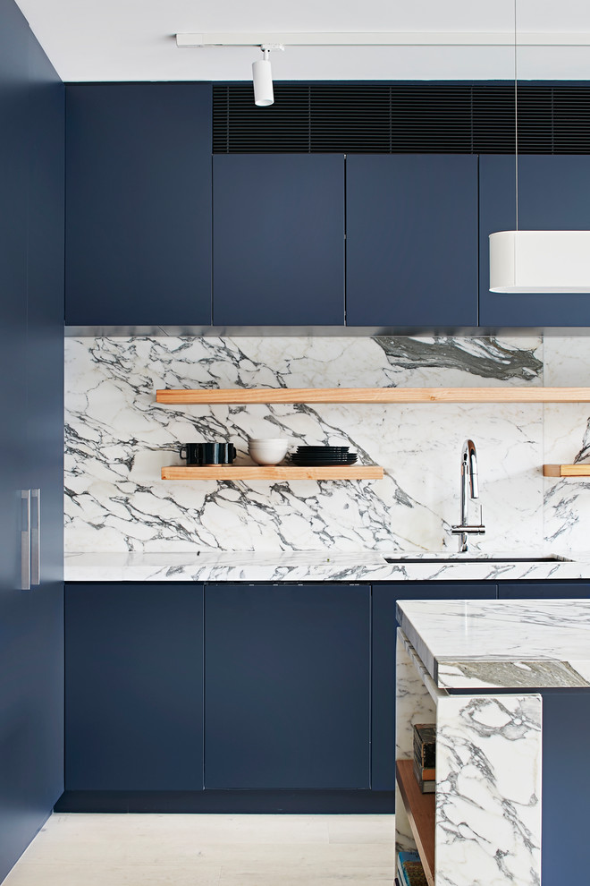 Foto på ett mellanstort funkis vit kök, med en undermonterad diskho, släta luckor, blå skåp, marmorbänkskiva, vitt stänkskydd, stänkskydd i marmor, rostfria vitvaror, ljust trägolv och en köksö