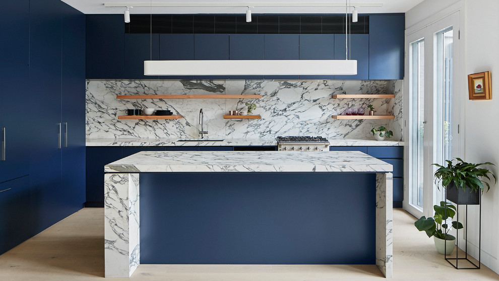 Modern inredning av ett mellanstort vit vitt kök, med en undermonterad diskho, släta luckor, blå skåp, marmorbänkskiva, vitt stänkskydd, stänkskydd i marmor, svarta vitvaror, ljust trägolv, en köksö och beiget golv
