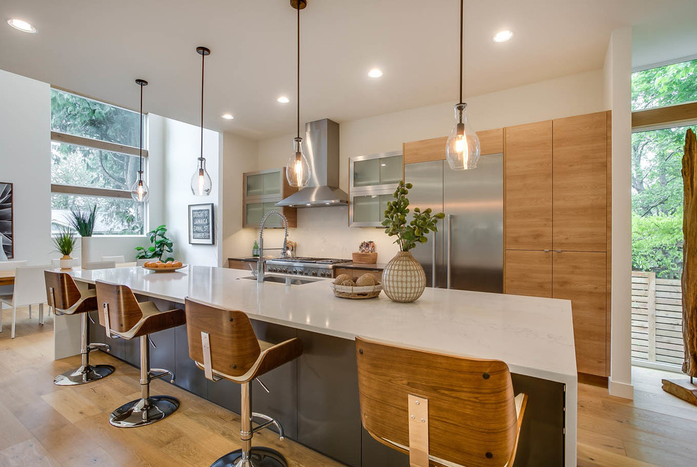 Moderne Wohnküche mit Unterbauwaschbecken, flächenbündigen Schrankfronten, hellen Holzschränken, Küchengeräten aus Edelstahl, hellem Holzboden, Kücheninsel und beigem Boden in Seattle