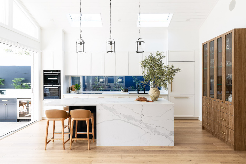 Inspiration for a large coastal galley kitchen in Sydney with shaker cabinets, white cabinets, marble worktops, an island, white worktops, a vaulted ceiling, a timber clad ceiling, window splashback, integrated appliances, medium hardwood flooring and brown floors.