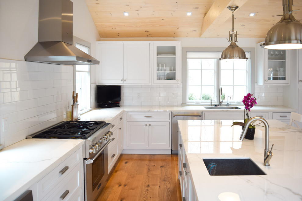 Medium sized country l-shaped kitchen/diner in New York with a submerged sink, shaker cabinets, white cabinets, marble worktops, white splashback, metro tiled splashback, stainless steel appliances, light hardwood flooring and an island.