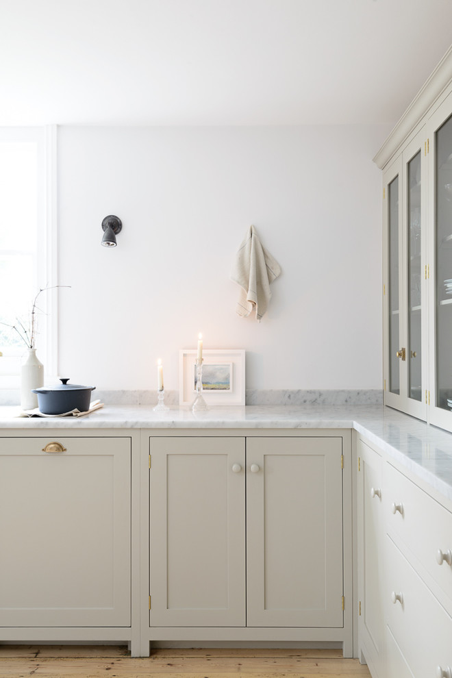 This is an example of a medium sized rural u-shaped open plan kitchen in Sussex with a belfast sink, shaker cabinets, grey cabinets, marble worktops, white splashback, metro tiled splashback, white appliances, light hardwood flooring and an island.