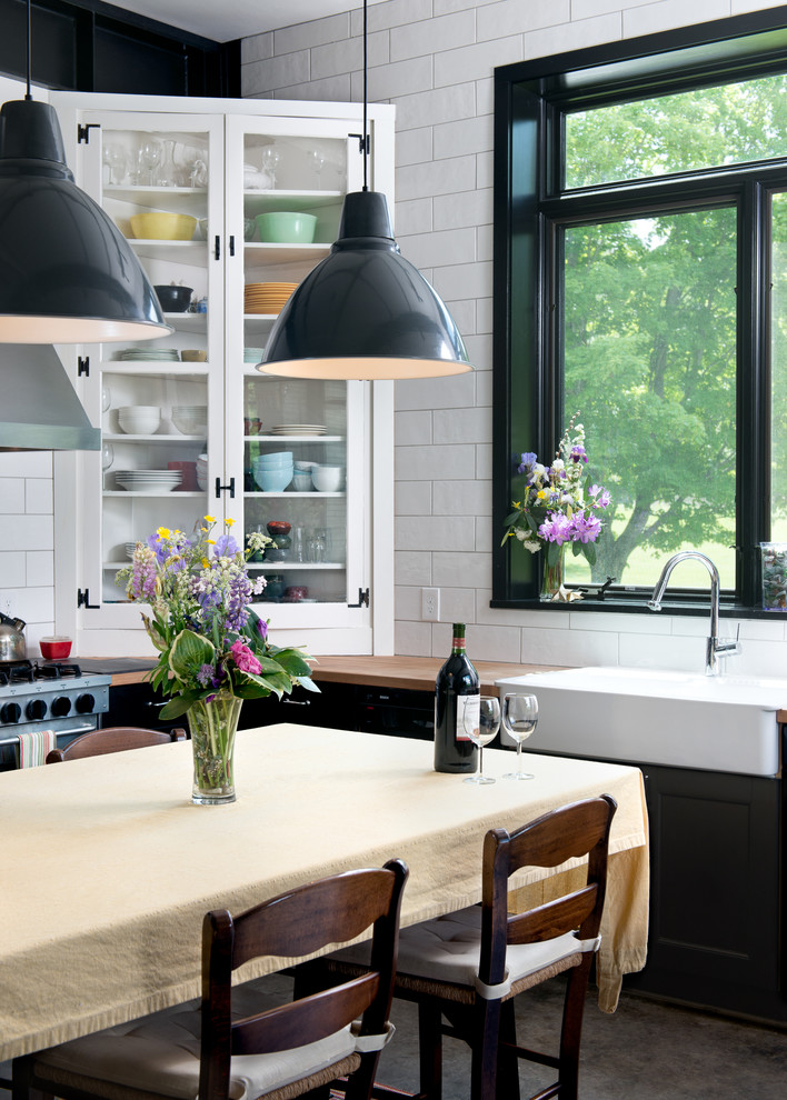 На фото: кухня в современном стиле с обеденным столом, с полувстраиваемой мойкой (с передним бортиком), стеклянными фасадами, деревянной столешницей, белым фартуком, фартуком из плитки кабанчик и черно-белыми фасадами