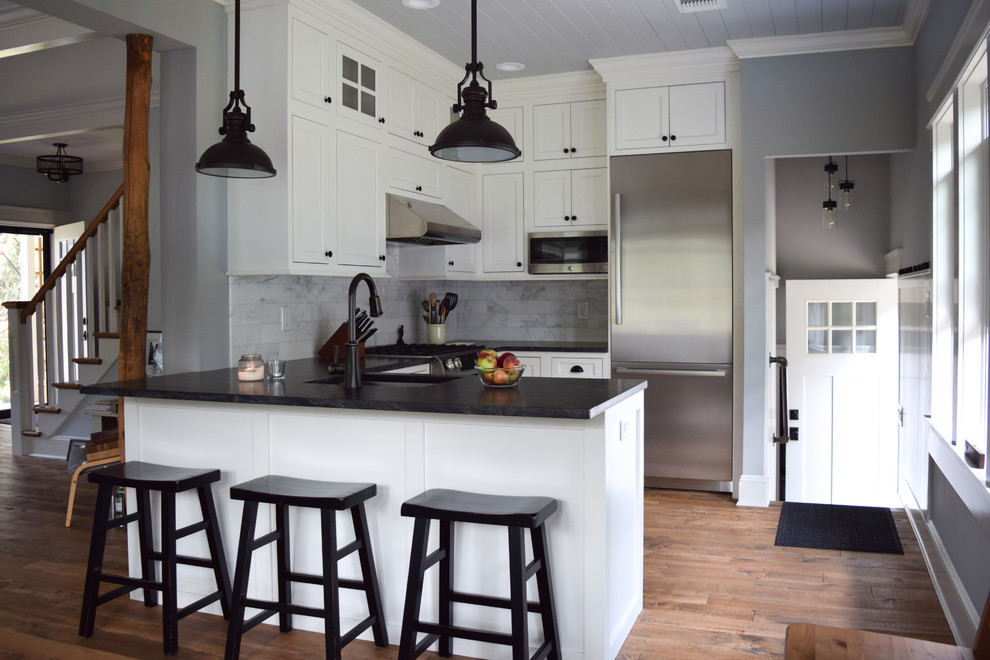 Foto på ett litet lantligt kök, med en undermonterad diskho, luckor med profilerade fronter, vita skåp, bänkskiva i täljsten, stänkskydd i marmor, rostfria vitvaror, mellanmörkt trägolv och en halv köksö