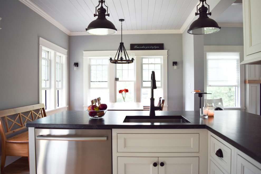 Foto på ett litet lantligt kök, med en undermonterad diskho, luckor med profilerade fronter, vita skåp, bänkskiva i täljsten, stänkskydd i marmor, rostfria vitvaror, mellanmörkt trägolv och en halv köksö