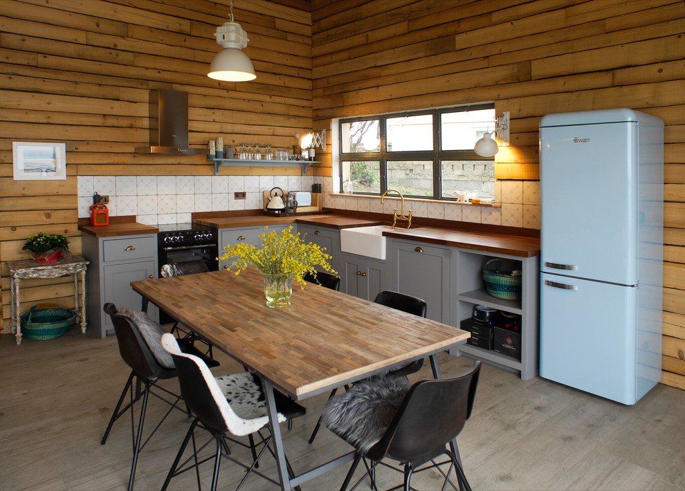 This is an example of a rural l-shaped kitchen/diner in London with a belfast sink, shaker cabinets, grey cabinets, wood worktops, white splashback, no island and grey floors.