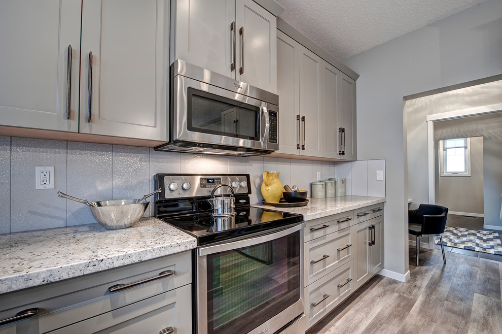 Foto på ett mellanstort lantligt kök, med en dubbel diskho, luckor med infälld panel, grå skåp, granitbänkskiva, vitt stänkskydd, stänkskydd i keramik, rostfria vitvaror, mellanmörkt trägolv och en köksö