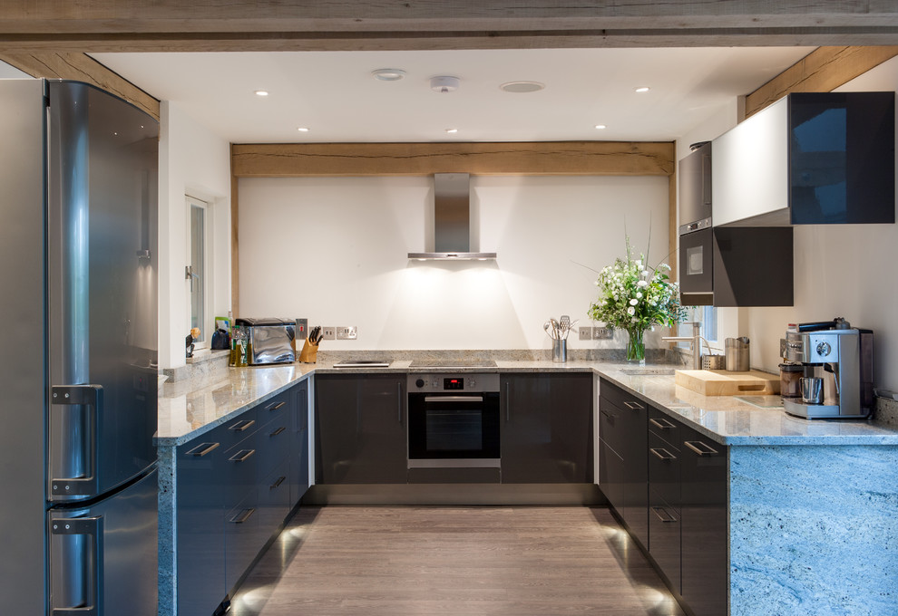 Mittelgroße Moderne Küche ohne Insel in U-Form mit flächenbündigen Schrankfronten, Küchengeräten aus Edelstahl, braunem Holzboden und Granit-Arbeitsplatte in Devon
