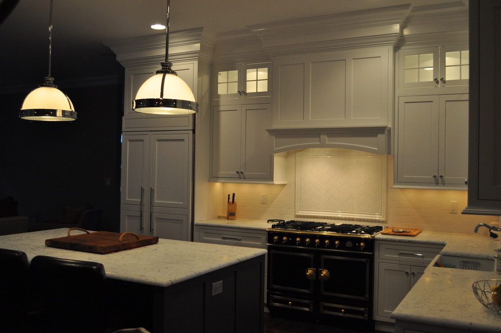 Example of a classic l-shaped dark wood floor eat-in kitchen design in New York with a farmhouse sink, recessed-panel cabinets, white cabinets, marble countertops, white backsplash, ceramic backsplash, stainless steel appliances and an island