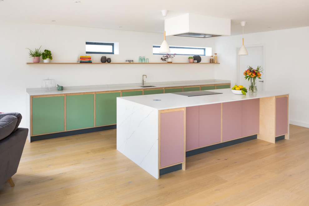 This is an example of a medium sized contemporary single-wall open plan kitchen in Other with an integrated sink, flat-panel cabinets, green cabinets, quartz worktops, white splashback, engineered quartz splashback, black appliances, light hardwood flooring, an island and white worktops.