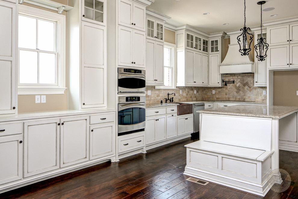 Inspiration for a transitional l-shaped open concept kitchen remodel in Louisville with a farmhouse sink, flat-panel cabinets, distressed cabinets, granite countertops, beige backsplash, stone tile backsplash and stainless steel appliances