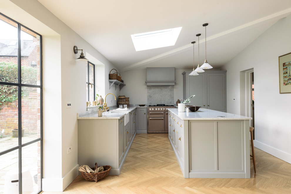 Large traditional l-shaped open plan kitchen in Other with a belfast sink, shaker cabinets, grey cabinets, marble worktops, white splashback, marble splashback, coloured appliances, light hardwood flooring and an island.
