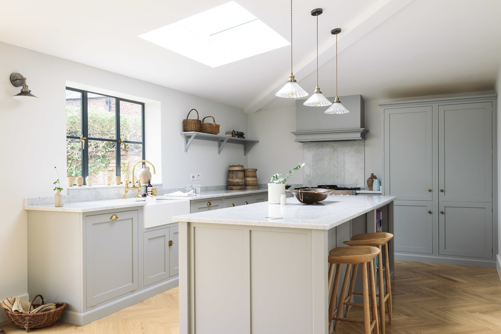 Design ideas for a large classic l-shaped kitchen in Other with a belfast sink, shaker cabinets, grey cabinets, marble worktops, white splashback, marble splashback, light hardwood flooring, an island and beige floors.