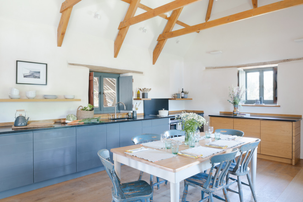 Large rural l-shaped open plan kitchen in Other with flat-panel cabinets, granite worktops, black splashback, stainless steel appliances, medium hardwood flooring, brown floors, black worktops, a submerged sink, blue cabinets and no island.