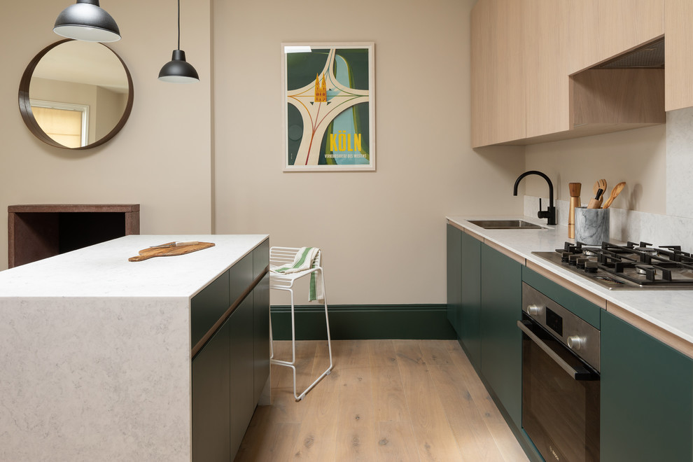 This is an example of a scandinavian kitchen in London with a double-bowl sink, flat-panel cabinets, green cabinets, white splashback, light hardwood flooring, an island, beige floors and white worktops.
