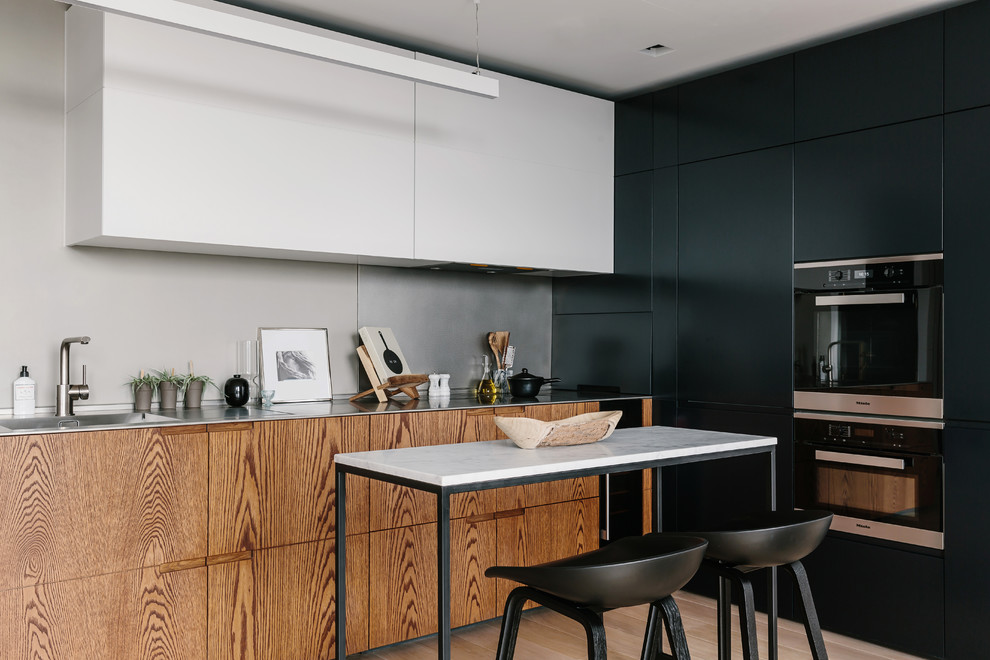Bild på ett funkis kök, med en integrerad diskho, skåp i mellenmörkt trä, bänkskiva i rostfritt stål, släta luckor, en köksö, beiget golv och grått stänkskydd