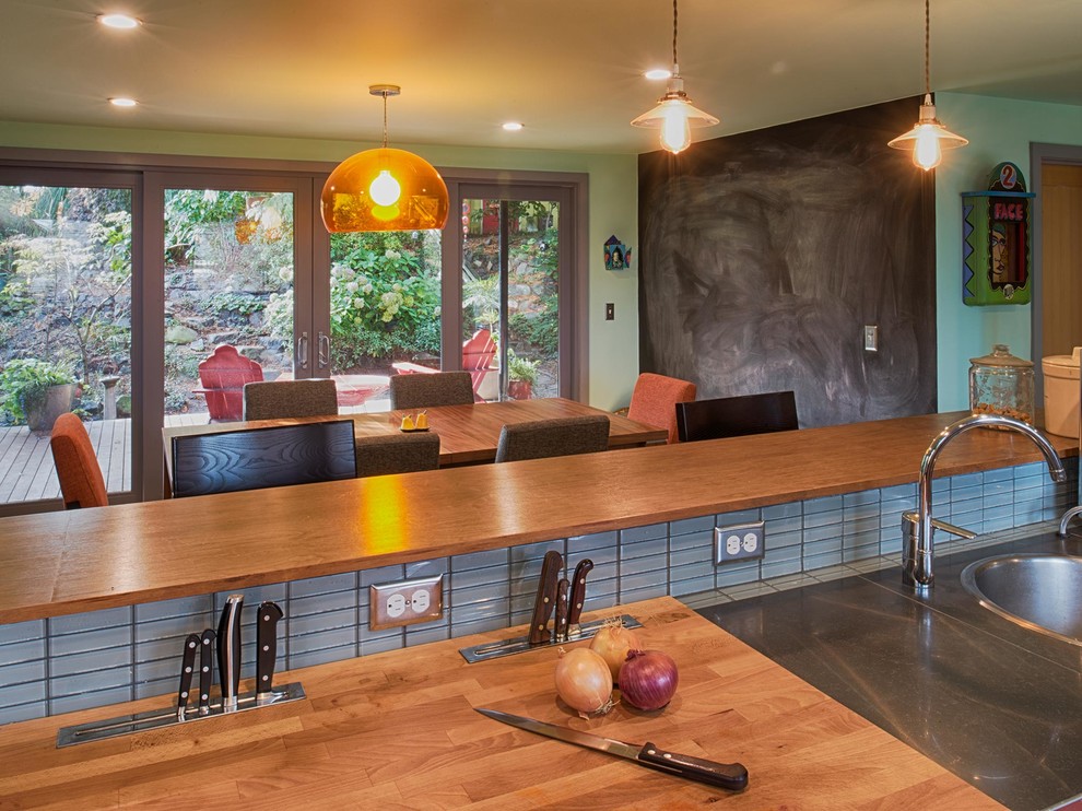 This is an example of a medium sized contemporary u-shaped open plan kitchen in Seattle with a single-bowl sink, flat-panel cabinets, dark wood cabinets, grey splashback, glass tiled splashback, stainless steel appliances, a breakfast bar and wood worktops.