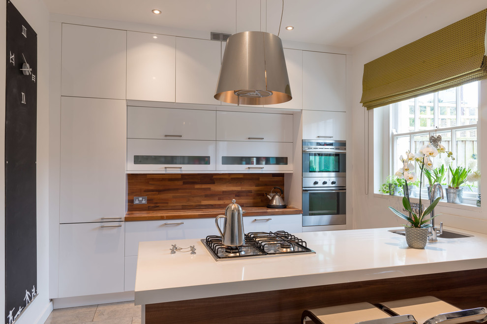 Modern single-wall open plan kitchen in Devon with a built-in sink, flat-panel cabinets, white cabinets, wood worktops, brown splashback, wood splashback, stainless steel appliances, porcelain flooring and an island.