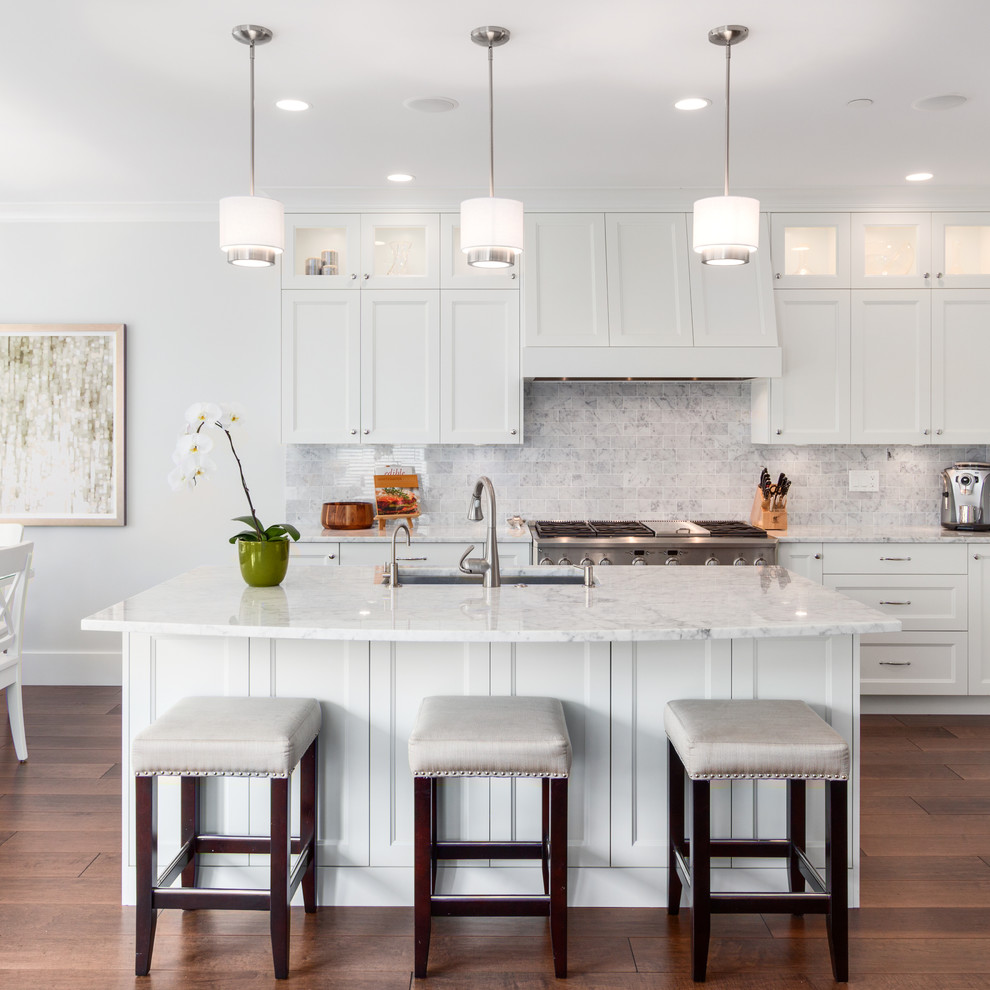 Example of a large transitional l-shaped medium tone wood floor open concept kitchen design in Vancouver with an undermount sink, recessed-panel cabinets, white cabinets, marble countertops, white backsplash, stone tile backsplash, stainless steel appliances and an island