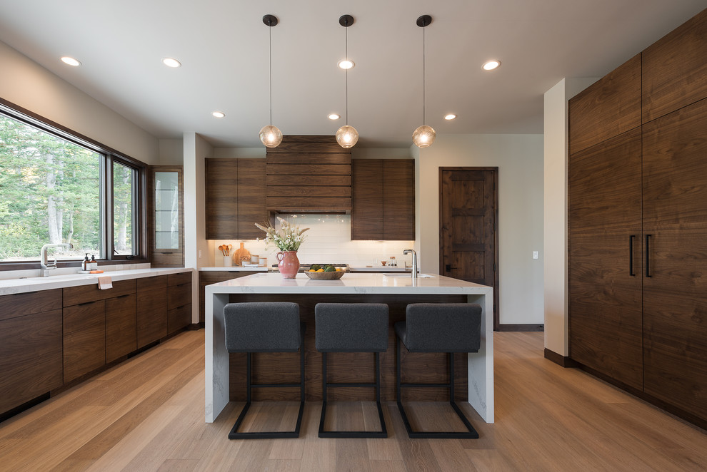 Moderne Küche mit Unterbauwaschbecken, flächenbündigen Schrankfronten, dunklen Holzschränken, Küchenrückwand in Weiß, Elektrogeräten mit Frontblende, hellem Holzboden und Kücheninsel in Salt Lake City