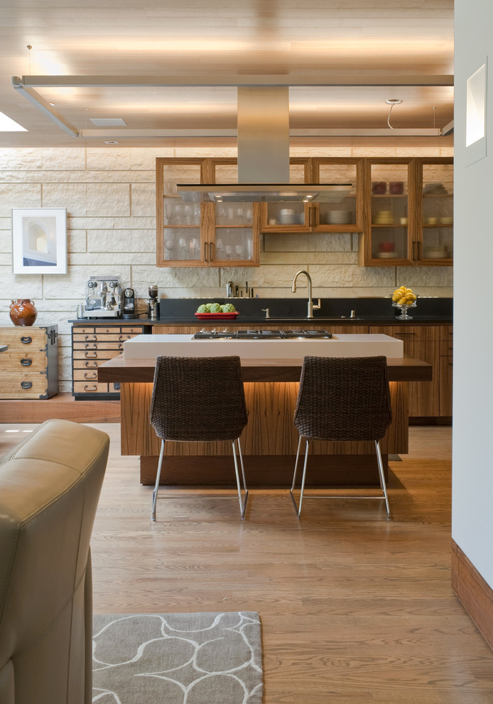 На фото: кухня-гостиная в современном стиле с стеклянными фасадами, фасадами цвета дерева среднего тона, деревянной столешницей и черным фартуком с