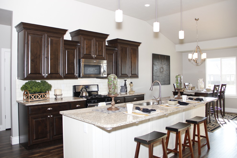 Eat-in kitchen - mid-sized traditional single-wall dark wood floor eat-in kitchen idea in Salt Lake City with a single-bowl sink, recessed-panel cabinets, dark wood cabinets, granite countertops, white backsplash, ceramic backsplash, stainless steel appliances and an island