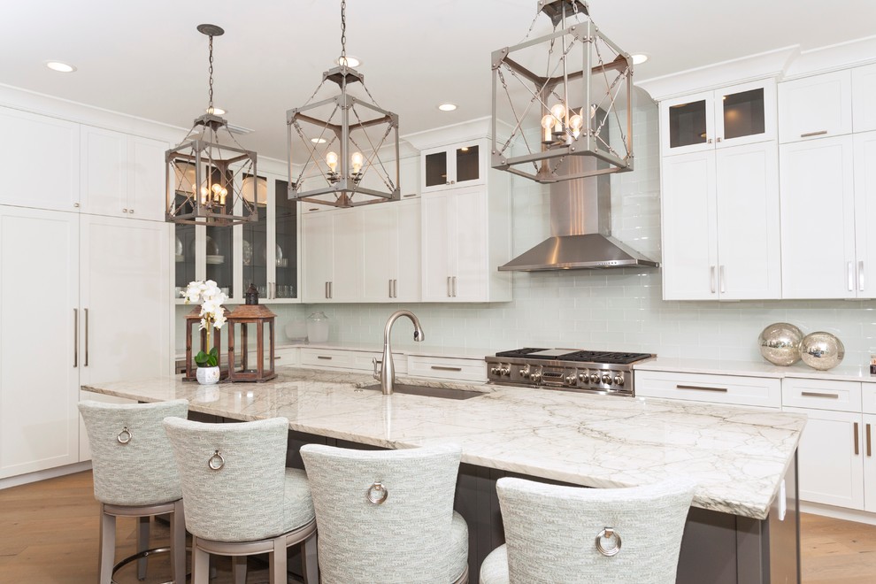 Traditional l-shaped kitchen in Miami with a submerged sink, shaker cabinets, white cabinets, white splashback, glass tiled splashback, stainless steel appliances, light hardwood flooring, an island and beige floors.